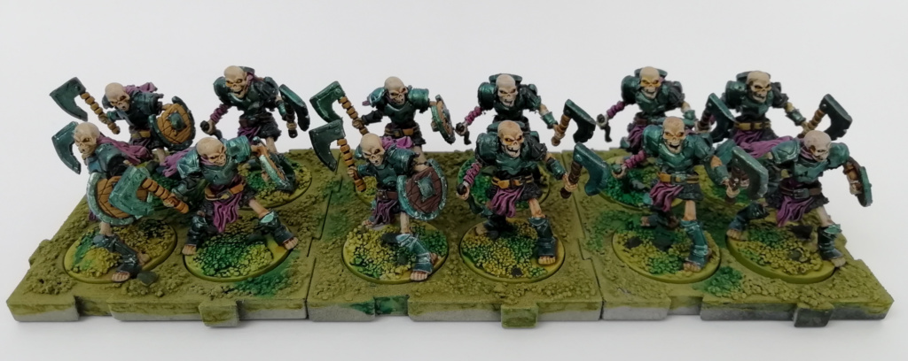 Showcase Runewars Tabletop Miniaturen: Untote Waiqar Skelett Armee: Infanterie mit Äxten, bemalt im Farbschema Blau-Metallic und Violett auf grünen Bases