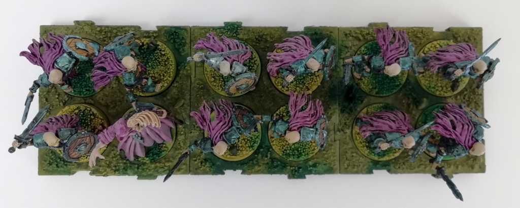 Showcase Runewars Tabletop Miniaturen: Untote Waiqar Skelett Armee: Nekromant und Wiederbelebte mit Schwert und Schild, bemalt im Farbschema Blau-Metallic und Violett auf grünen Bases