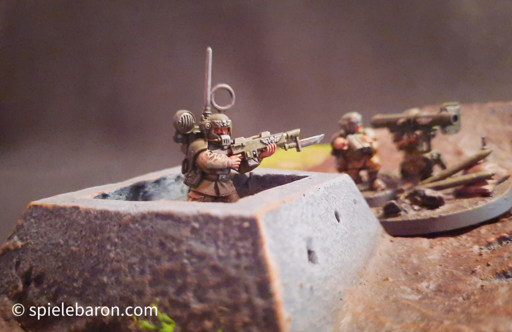 40k Showcase Foto: Astra Militarum, bemalte Imperial Outpost Spielplatte von Forge World, darauf Miniaturen von Infanterie Soldaten und Heavy Weapons Team, gehobener Standard