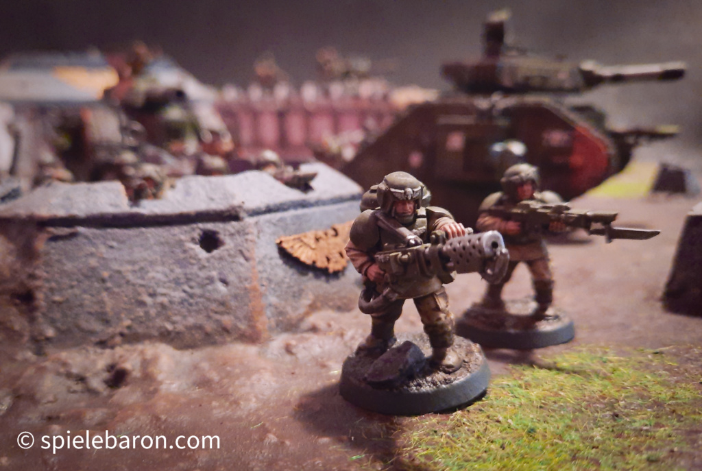 40k Showcase Foto: Astra Militarum, bemalte Imperial Outpost Spielplatte von Forge World, darauf Miniaturen von Leman Russ Panzern und Infanterie Soldaten, gehobener Standard