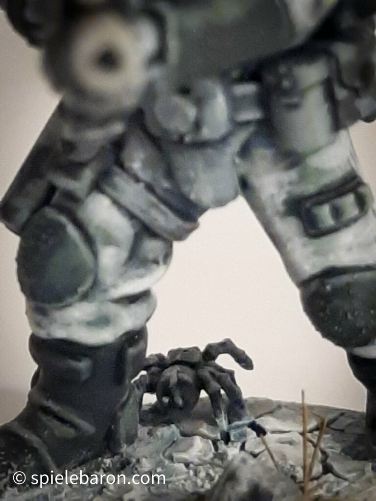 Foto eines Space Marine Primaris Scouts mit Boltgewehr in Winter-Camouflage, bemalt mit Winterbase vor weißem Hintergrund; Detail Spinne auf Schneeboden