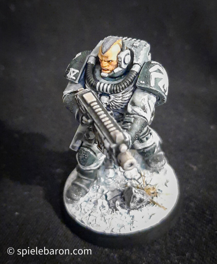 Foto eines Space Marine Primaris Scouts mit Boltgewehr in Winter-Camouflage, bemalt mit Winterbase vor schwarzem Hintergrund; von vorne oben seitlich