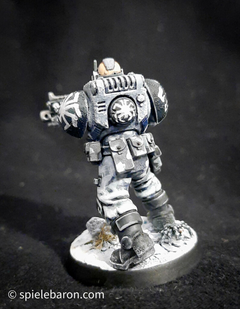 Foto eines Space Marine Primaris Scouts mit Boltgewehr in Winter-Camouflage, bemalt mit Winterbase vor schwarzem Hintergrund; von hinten