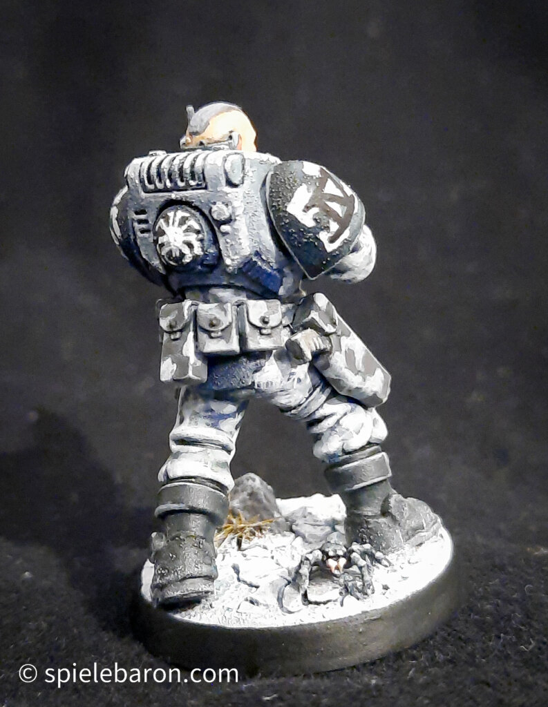 Foto eines Space Marine Primaris Scouts mit Boltgewehr in Winter-Camouflage, bemalt mit Winterbase vor schwarzem Hintergrund; von hinten